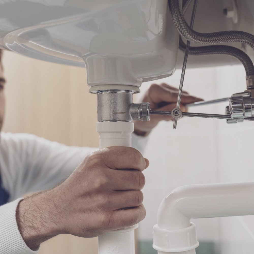 Plumber fixing the drain under a sink at home