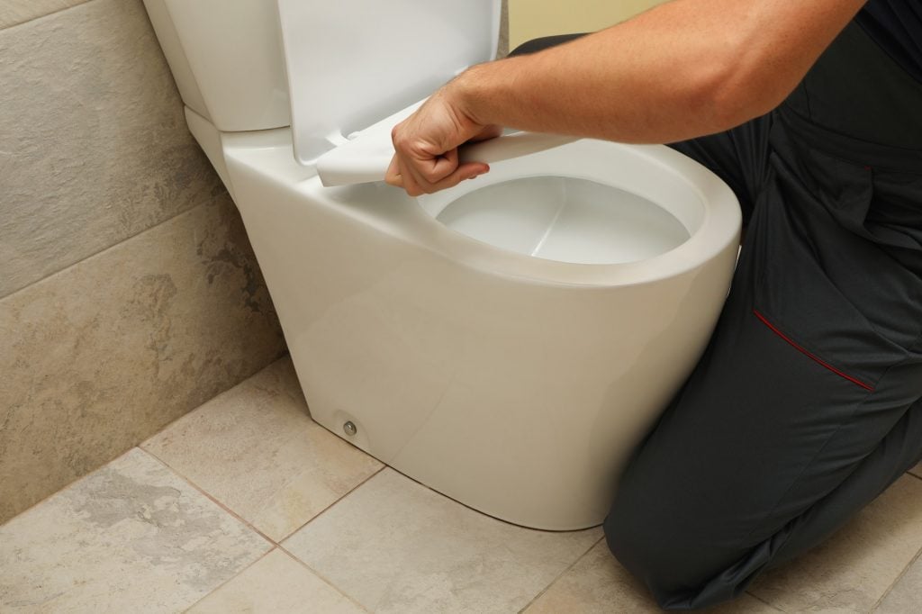 The plumber in overalls fixes the toilet