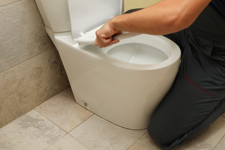 The plumber in overalls fixes the toilet
